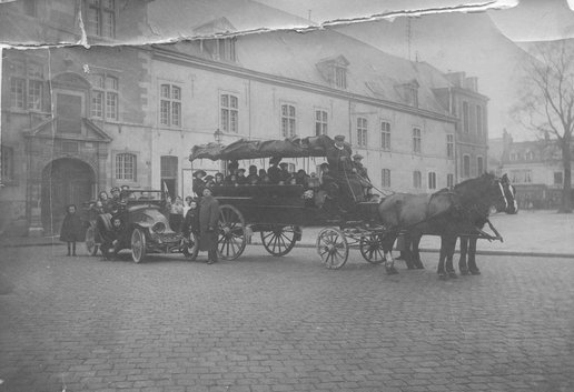 Groupe composé d'enfants, s'apprêtant à partir, entourés d'adultes, posant devant la façade de l’Hospice général, place Museux